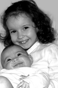 Two happy smiling sisters - a toddler holding a little cute baby